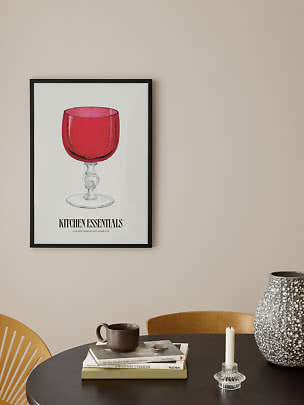 Ingelijste poster met rode bokaal op witte achtergrond boven een donkere tafel.