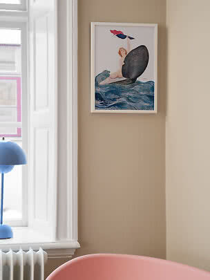 Framed art print of a mermaid on ocean waves hanging on a beige wall