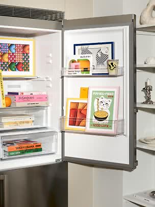 Open koelkast ingericht met kunstprints, boeken en tijdschriften op planken en in de deur