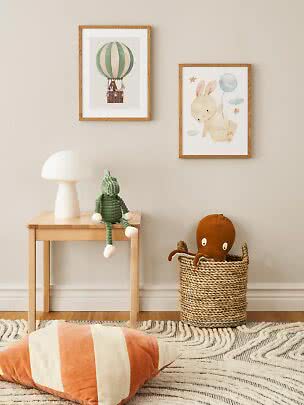 Kids room with two framed animal prints, wooden side table, white lamp, plush toy and basket
