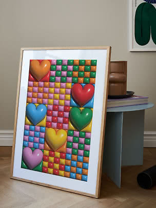 Affiche d’art colorée encadrée avec grands cœurs et motif à carreaux, posée contre une table