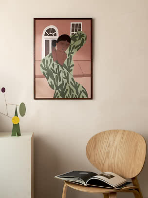 Gerahmtes Poster mit stilisierter Frau in grün gemustertem Kleid an beiger Wand über Holzstuhl