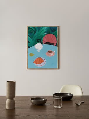 Framed wall art of a croissant, cup, pear and flowers on a blue table with leafy background