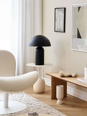 Sort bordlampe med kuppelskærm på rundt sidebord i lys, moderne stue.