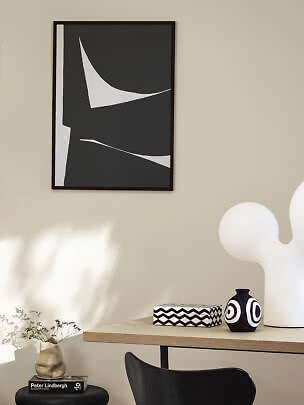 Poster astratto bianco e nero incorniciato su parete beige sopra un tavolo con vaso e decorazioni