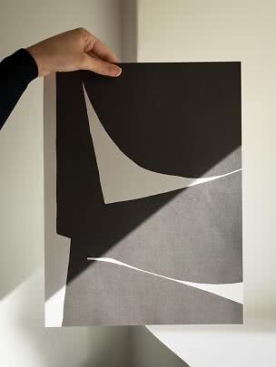 Mano che tiene un poster astratto bianco e nero con forme organiche su parete chiara