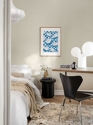 Chambre lumineuse avec lit, bureau, chaise noire, lampe blanche et affiche bleue encadrée