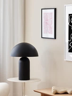 Schwarze Tischlampe mit kuppelförmigem Schirm auf kleinem rundem Beistelltisch in hellem Raum