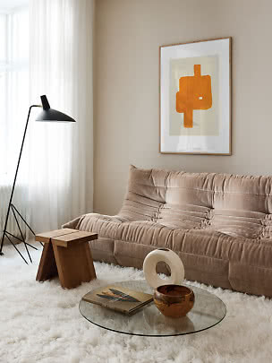 Beige sofa i stuen med glasbord, sort gulvlampe og abstrakt orange vægkunst