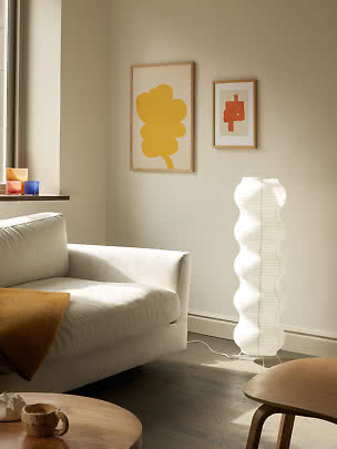 Hvid bølgeformet gulvlampe ved beige sofa i lyst, moderne stue