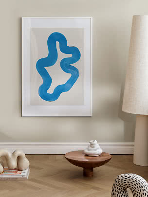 Framed abstract print with blue organic shape on a beige wall in a modern room