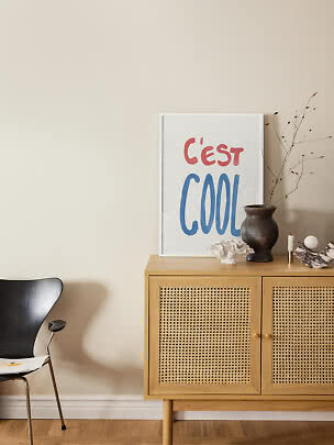 Plakat med teksten "C'est Cool" står på skænk med vase og dekorationer i lyst rum