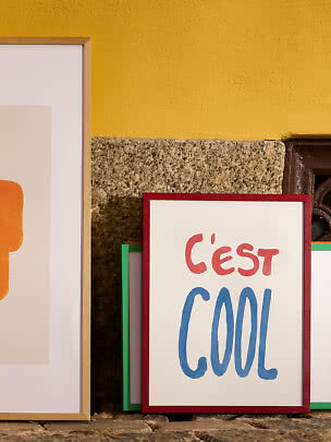 Indrammede plakater lænet op ad gul gulvæg, en med teksten "C'est cool".