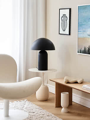 Sort bordlampe med kuppelskærm på rundt sidebord i lyst, moderne stuehjørne