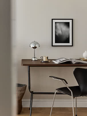Bureau minimaliste avec lampe chromée, tasse, livre ouvert et chaise noire sur mur beige