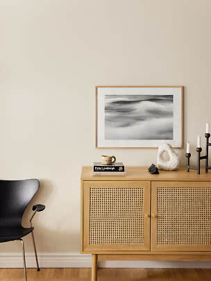 Madia in legno chiaro con ante in rattan, sedia nera e decori sotto foto in bianco e nero