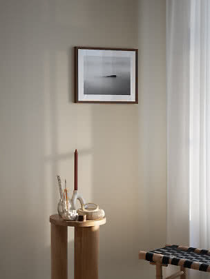 Indrammet sort-hvidt foto på beige væg over træbord med lys og små dekorationer