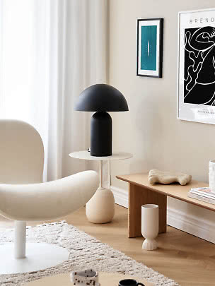 Black dome table lamp on a round side table in a bright, modern living room corner.