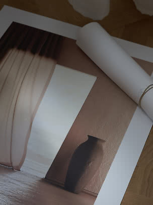 Poster d’arte arrotolato con vaso marrone e tende su pavimento in legno
