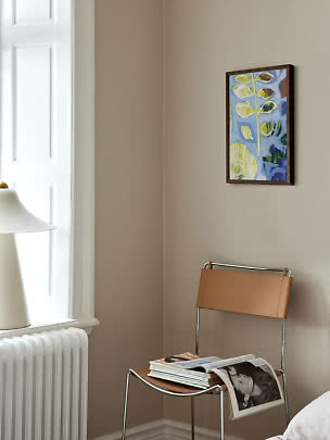 Framed abstract artwork on a beige wall above a leather chair in a bright corner