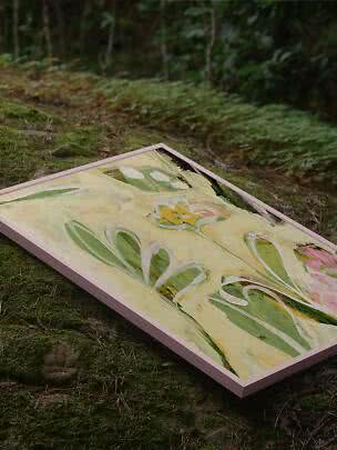 Indrammet abstrakt blomstermaleri med grønne og rosa toner, placeret på mosbund i skov