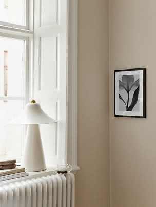 Piccola stampa floreale con cornice nera su parete beige accanto a finestra e lampada bianca