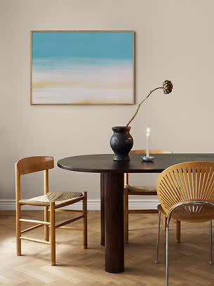 Abstract beach print in blue and sand tones in a light wood frame above a dining table