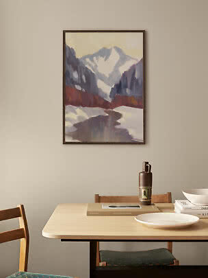 Framed painting of snowy mountains and a winding river hanging above a dining table