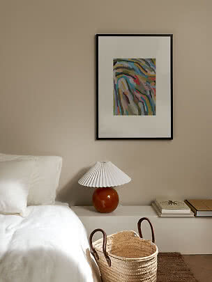 Cozy bedroom with white bed, pleated lamp, basket, and colorful abstract wall art