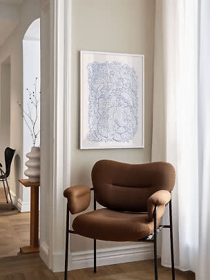 Framed abstract blue line drawing above a brown lounge chair by a bright window