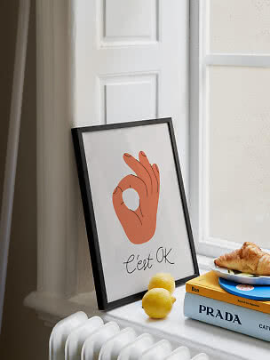 Oprawiony plakat z gestem dłoni przy oknie, z cytrynami, książkami i croissantem na parapecie