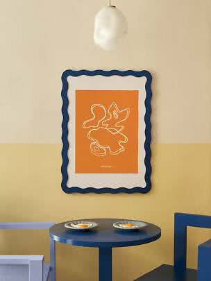 Orange abstrakt plakat i bølget blå ramme over rundt blåt bord med to tallerkener