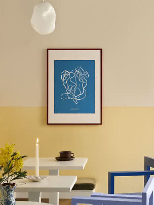 Framed blue abstract poster with white line drawing on a yellow wall above a table