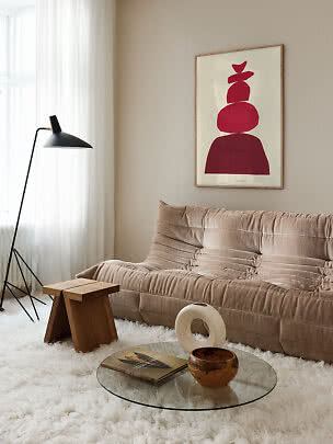 Stue med beige sofa, sort gulvlampe, rundt glasbord og rød abstrakt plakat på væggen