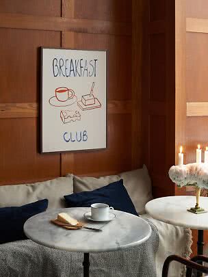 Poster incorniciato "Breakfast Club" su parete in legno sopra tavolino con tazza e burro.