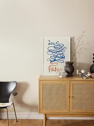 Sideboard aus hellem Holz mit Geflechtüren, Poster, dunkler Vase und Dekoobjekten