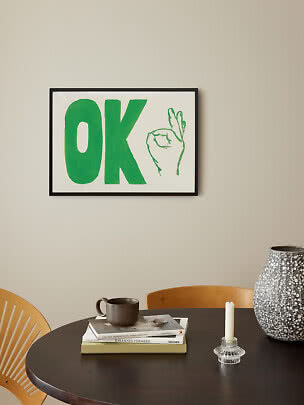 Indrammet plakat med grønt "OK" og håndtegn på lys væg over rundt bord.