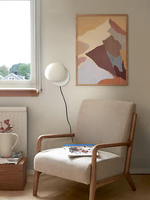 Fauteuil lounge beige en bois à côté d'une applique et d'une affiche abstraite