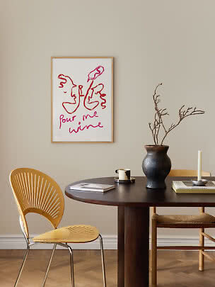 Affiche encadrée avec visages abstraits et texte rose au-dessus d'une table à manger ronde