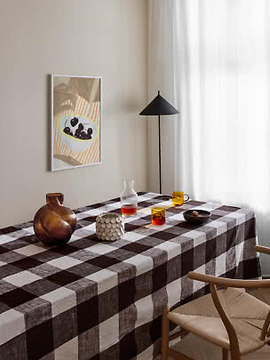 Esstisch mit braun karierter Tischdecke, Gläsern, Vase und schwarzer Stehlampe am Fenster