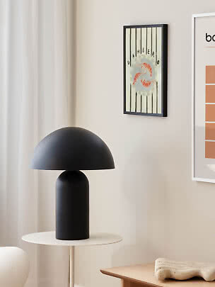 Schwarze Tischlampe mit rundem Schirm auf weißem Beistelltisch in hellem, modernem Raum