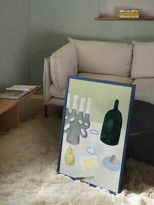 Indrammet stillebenmaleri lænet mod sofabord ved beige sofa på lyst, blødt tæppe