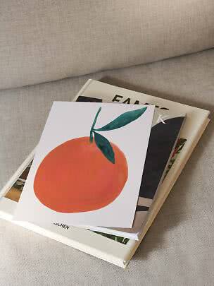 Cartolina illustrata con arancia sopra due libri su un divano beige