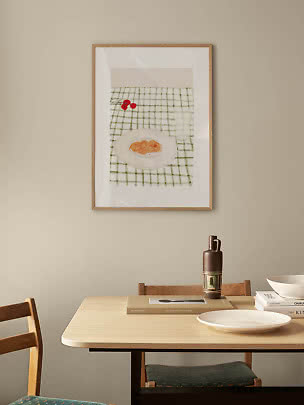 Indrammet kunsttryk med tallerken og kirsebær over ternet dug på beige væg