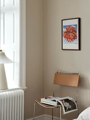 Gerahmtes Basketballbild an beiger Wand über einem Stuhl mit Magazinen in heller Ecke
