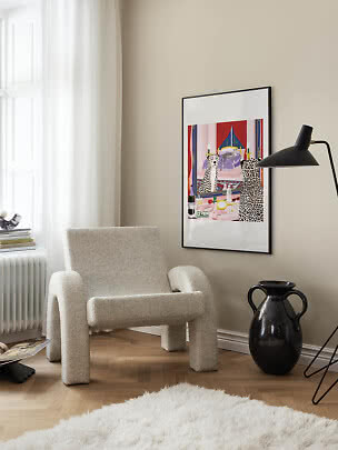 Gerahmter farbiger Kunstdruck an beige Wand über Bouclé-Sessel in heller moderner Ecke