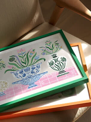 Bloemenprint in groene lijst op beige stoel, boven op een oranje lijst in zonlicht