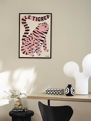 Affiche encadrée avec tigre rose et texte « Le Tigre » sur mur beige au-dessus d'une table