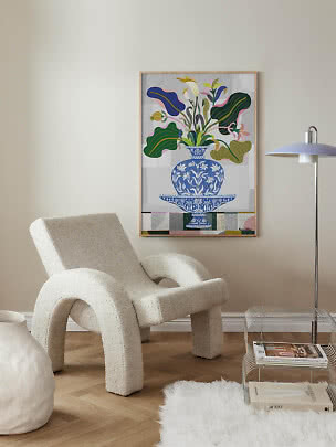 Moderne woonkamer met bouclé fauteuil en kleurrijke bloemenposter in houten lijst aan de muur