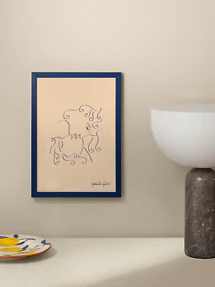 Gerahmte Linienzeichnung einer Umarmung im blauen Rahmen an beigefarbener Wand neben Tischlampe.